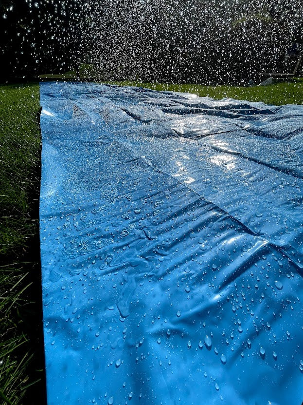 waterslide on the grass in the backyard with a hose spraying water across it