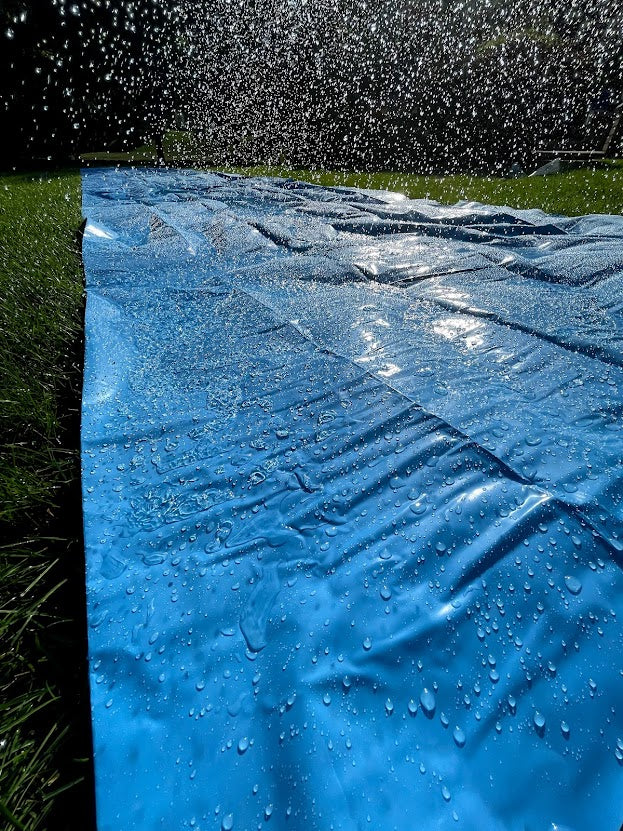 waterslide on the grass in the backyard with a hose spraying water across it